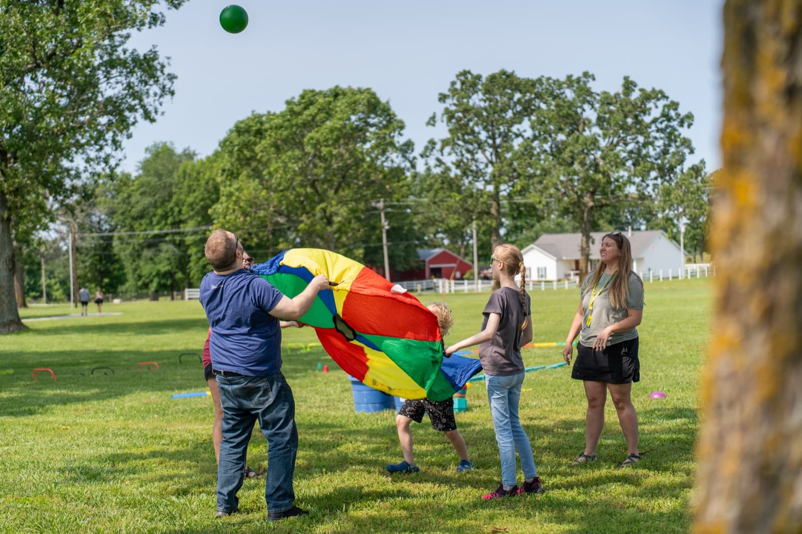 A group of families gathered around a rainbow parachute on the grass.