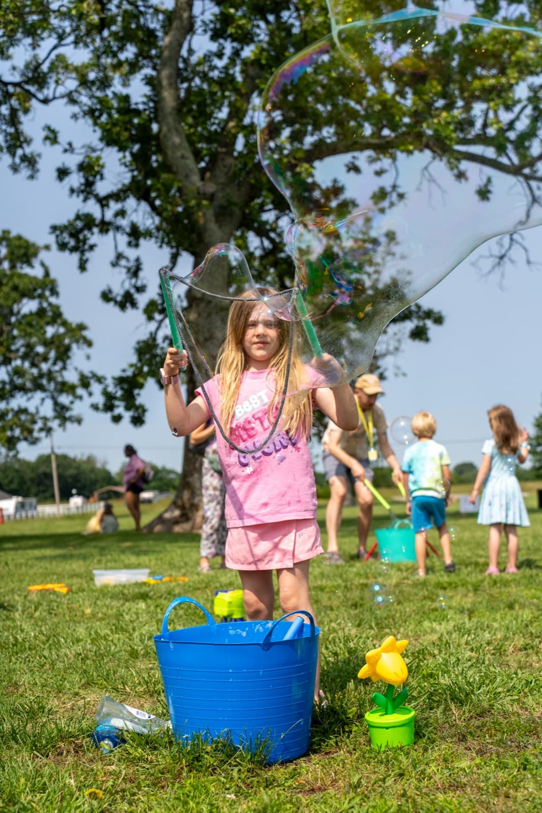 An adult smiling outdoors at a community event on a sunny day.