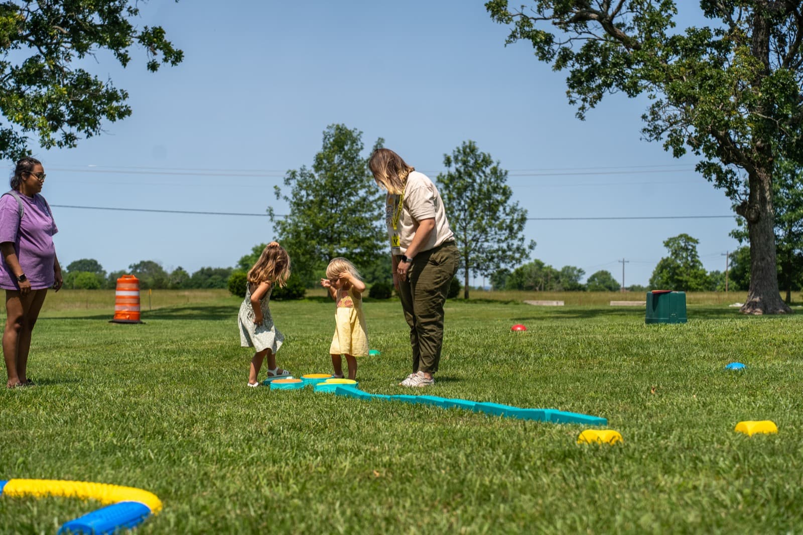An adult guides a child around a marked activity course on the grass.